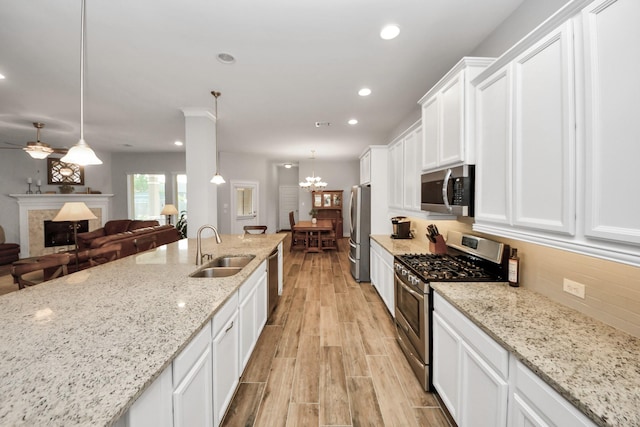 kitchen with stainless steel appliances, a sink, a high end fireplace, white cabinetry, and light wood-type flooring