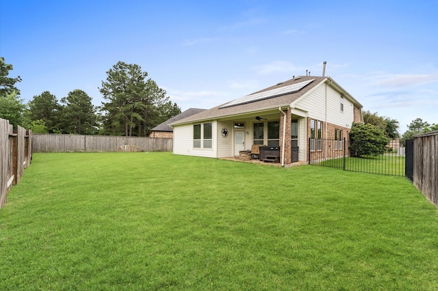 back of property with a lawn, a ceiling fan, roof mounted solar panels, and a fenced backyard