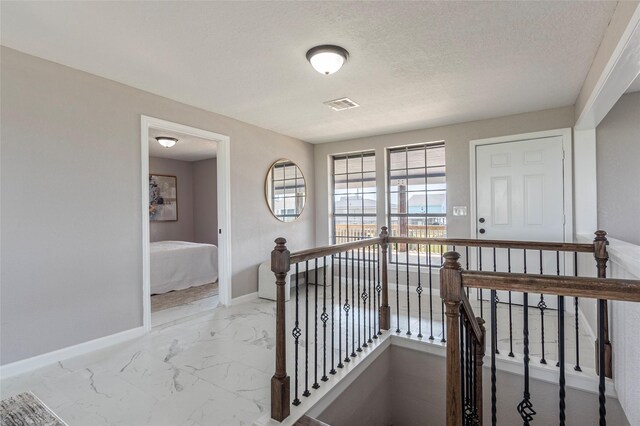 12928 John Reynolds Rd, Galveston, TX 77554 - hallway featuring an upstairs landing, a textured ceiling, visible vents, baseboards, and marble finish floor