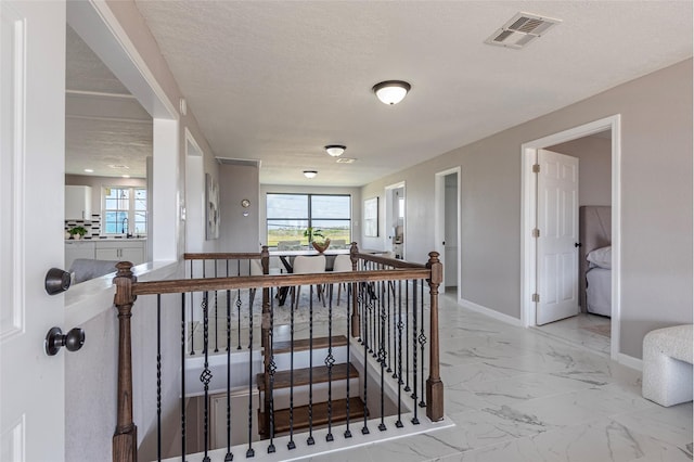 12928 John Reynolds Rd, Galveston, TX 77554 - hallway with a textured ceiling, baseboards, marble finish floor, visible vents, and an upstairs landing