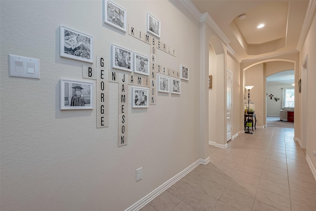 hall featuring crown molding, arched walkways, baseboards, and light tile patterned floors