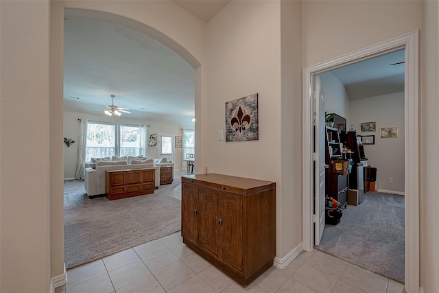 corridor featuring arched walkways, baseboards, light tile patterned flooring, and light colored carpet