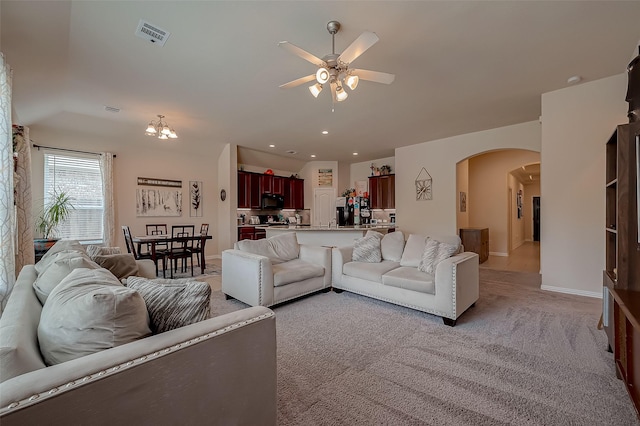 living area with visible vents, light colored carpet, arched walkways, baseboards, and ceiling fan with notable chandelier