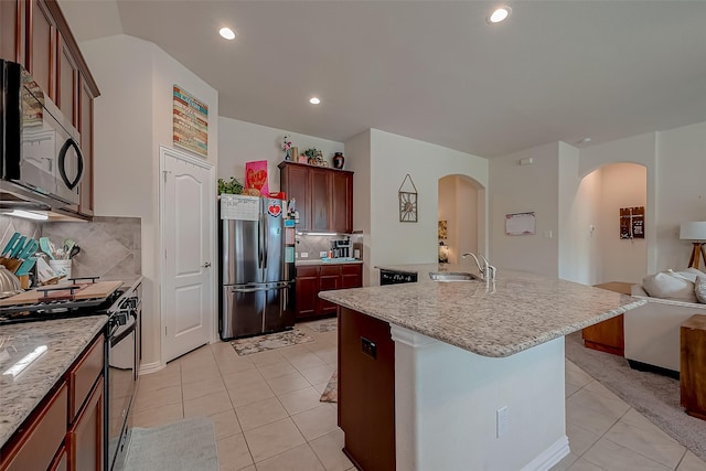 kitchen with appliances with stainless steel finishes, a sink, arched walkways, open floor plan, and light tile patterned floors