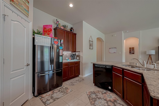 kitchen with arched walkways, a sink, light tile patterned floors, freestanding refrigerator, and black dishwasher