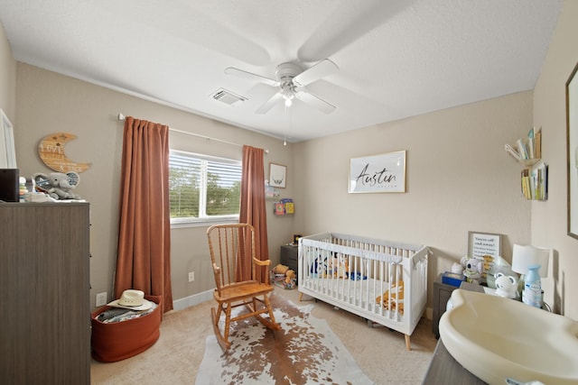 bedroom with carpet floors, a ceiling fan, a nursery area, and visible vents