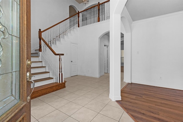 foyer entrance with crown molding, a high ceiling, arched walkways, stairs, and light tile patterned floors