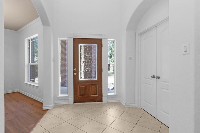 entrance foyer featuring baseboards, arched walkways, a healthy amount of sunlight, and ornamental molding
