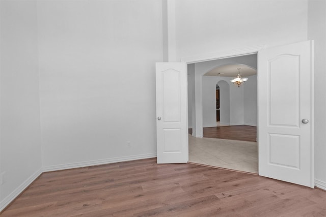 unfurnished room featuring arched walkways, baseboards, wood finished floors, and a high ceiling