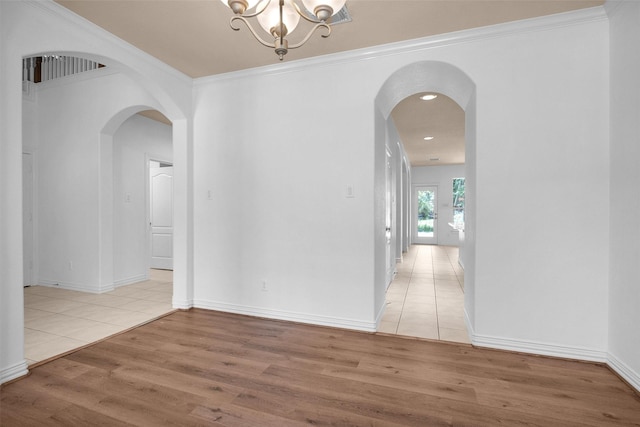 interior space with crown molding, a notable chandelier, arched walkways, light wood-style flooring, and baseboards