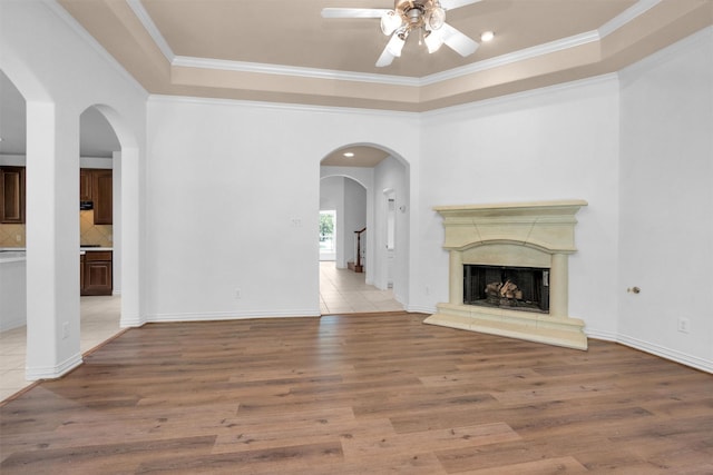 unfurnished living room featuring crown molding, a raised ceiling, a ceiling fan, and wood finished floors