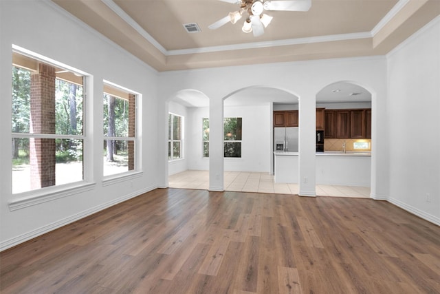 unfurnished living room featuring a ceiling fan, visible vents, crown molding, a tray ceiling, and light wood-style flooring