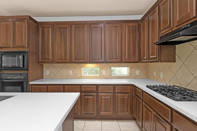 kitchen featuring light stone counters, tasteful backsplash, black appliances, and under cabinet range hood