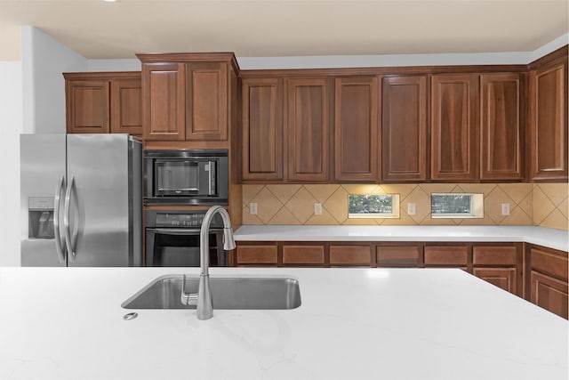 kitchen with light stone counters, a sink, black appliances, and tasteful backsplash