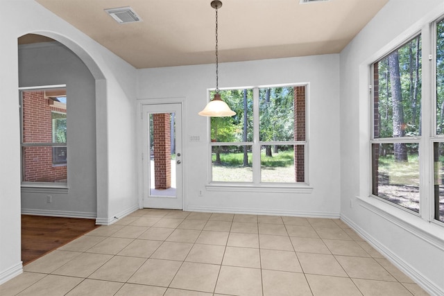 unfurnished dining area featuring arched walkways, baseboards, visible vents, and a wealth of natural light
