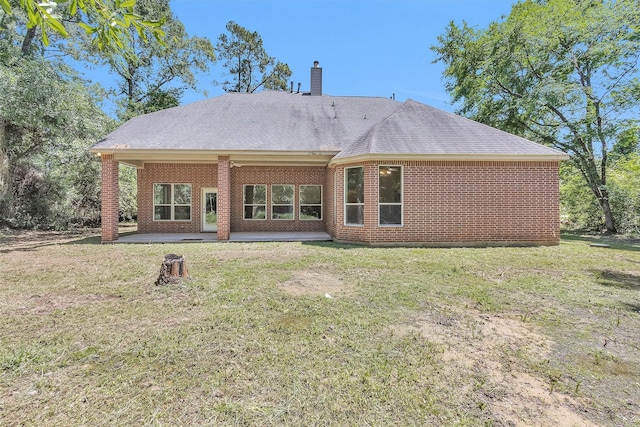 rear view of property with a lawn, a shingled roof, and a patio area