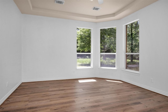 unfurnished room with visible vents, wood finished floors, and a raised ceiling
