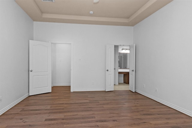 unfurnished bedroom featuring connected bathroom, a raised ceiling, and wood finished floors