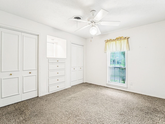 unfurnished bedroom featuring a textured ceiling, carpet, visible vents, two closets, and a ceiling fan