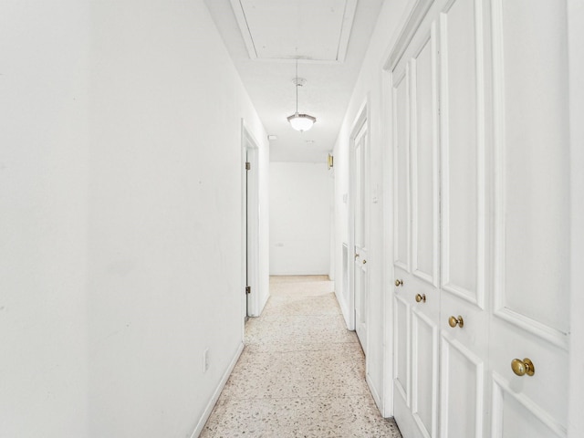 hall with attic access, baseboards, and light speckled floor