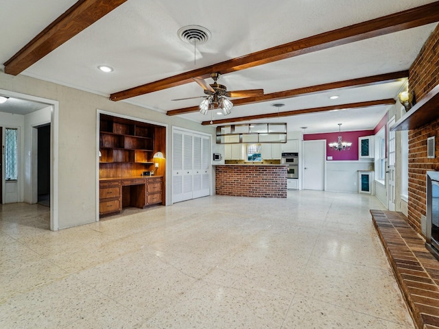 unfurnished living room with built in desk, ceiling fan with notable chandelier, a fireplace, visible vents, and beamed ceiling