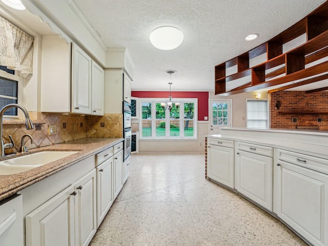 kitchen featuring baseboards, a chandelier, white cabinetry, and a sink