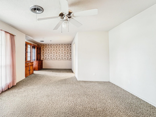 empty room featuring wallpapered walls, baseboards, ceiling fan, visible vents, and light colored carpet