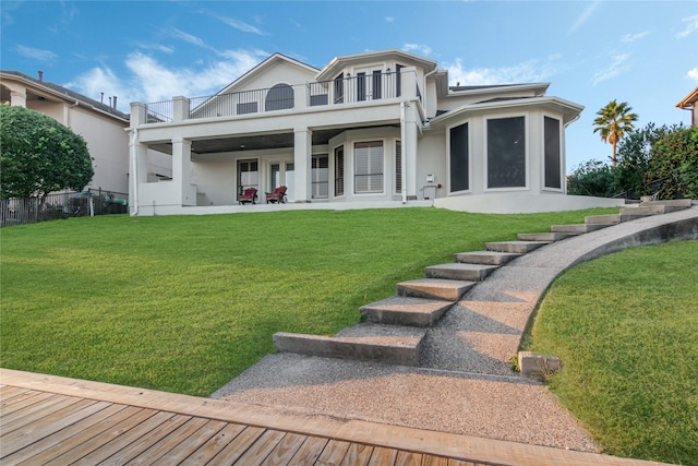 back of house featuring a lawn, a patio area, stucco siding, and a balcony