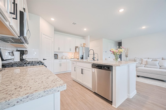 kitchen featuring a sink, appliances with stainless steel finishes, open floor plan, light wood-style floors, and decorative backsplash