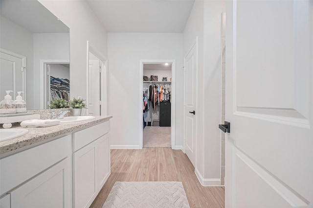 bathroom featuring double vanity, wood finished floors, a walk in closet, and a sink