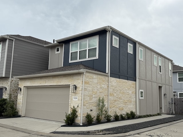 view of side of property featuring an attached garage, concrete driveway, and stone siding