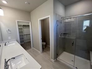 full bathroom featuring double vanity, a shower stall, toilet, and a sink