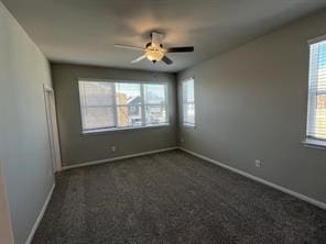 empty room featuring a ceiling fan, baseboards, and dark carpet