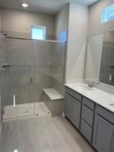 bathroom featuring wood finished floors, double vanity, a sink, and a stall shower