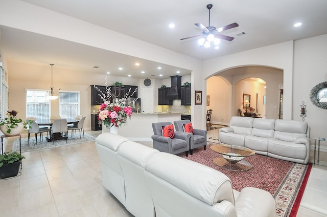 living room featuring baseboards, ceiling fan, arched walkways, light tile patterned flooring, and recessed lighting