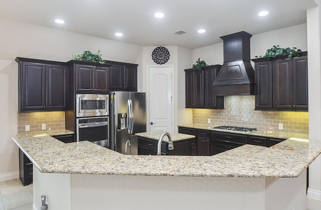 kitchen featuring premium range hood, visible vents, light stone countertops, appliances with stainless steel finishes, and a kitchen island
