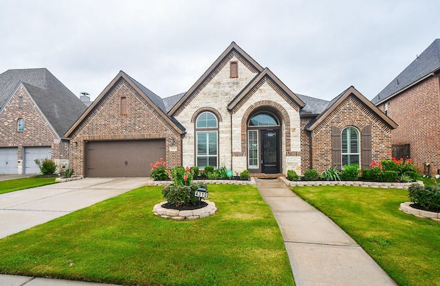 french country style house with stone siding, a garage, a front lawn, brick siding, and driveway