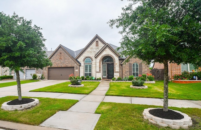 french country home with an attached garage, a front lawn, brick siding, and driveway