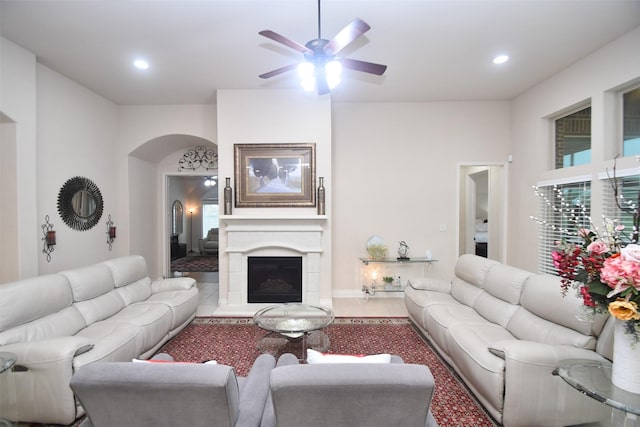 living room with ceiling fan, arched walkways, a fireplace with raised hearth, and recessed lighting