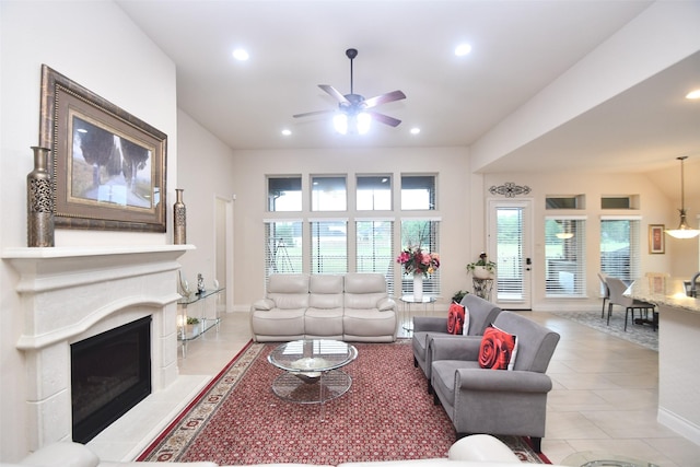 living area with light tile patterned floors, plenty of natural light, ceiling fan, and a fireplace with raised hearth
