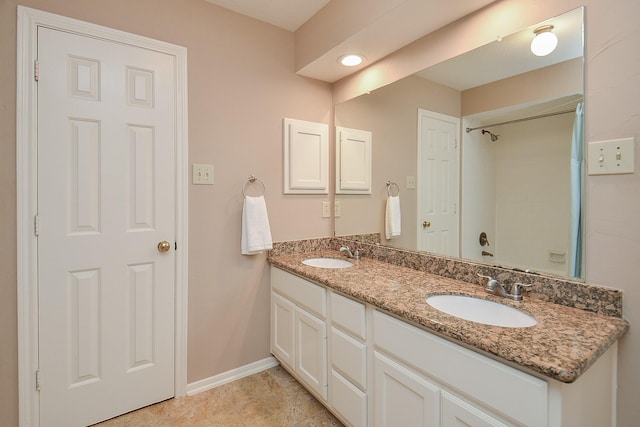 bathroom featuring a sink, baseboards, walk in shower, and double vanity