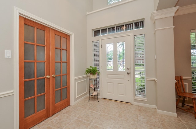foyer featuring light tile patterned floors, a decorative wall, and french doors