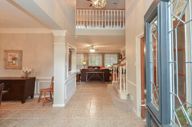 foyer featuring crown molding, light tile patterned flooring, a high ceiling, a ceiling fan, and stairway