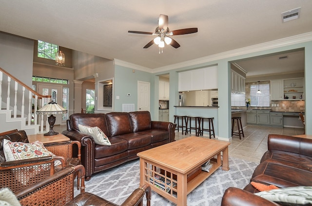 living area with decorative columns, a ceiling fan, visible vents, crown molding, and stairs