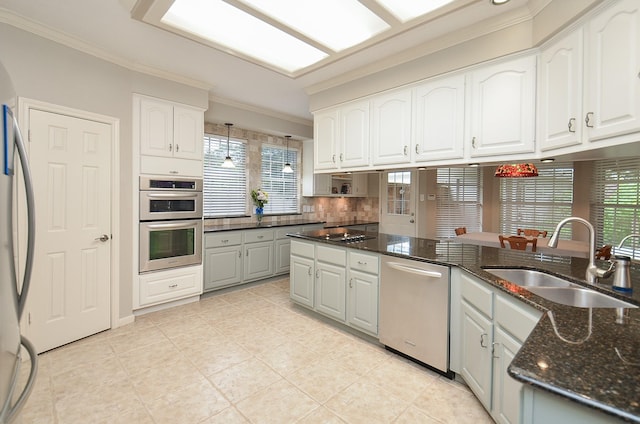 kitchen with crown molding, appliances with stainless steel finishes, a sink, dark stone countertops, and white cabinetry
