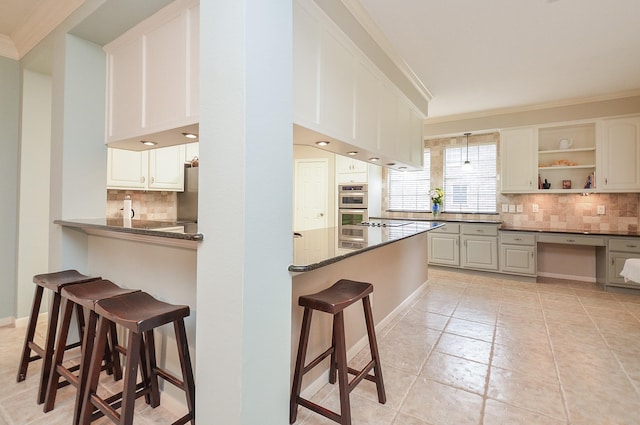 kitchen featuring double oven, a kitchen breakfast bar, a peninsula, tasteful backsplash, and ornamental molding