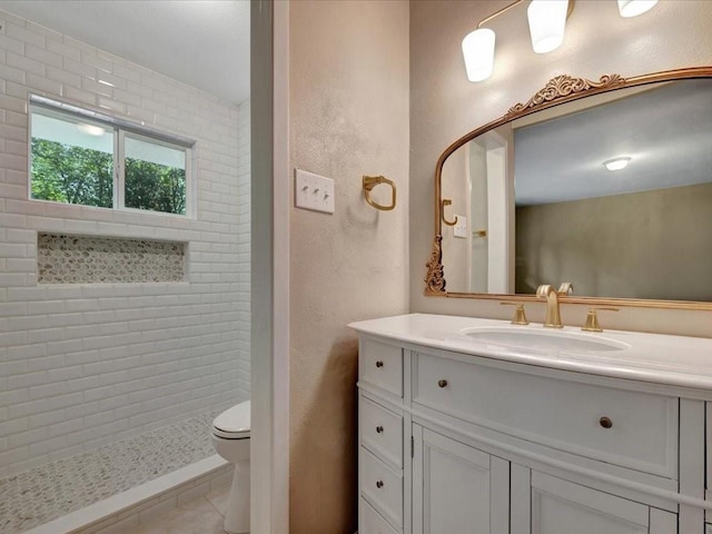 bathroom featuring vanity, tile patterned flooring, a tile shower, and toilet