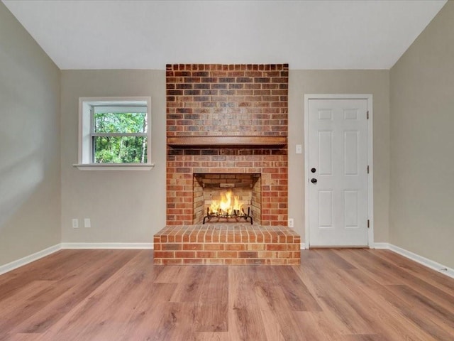 unfurnished living room featuring a brick fireplace, baseboards, and wood finished floors