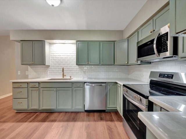 kitchen with a sink, appliances with stainless steel finishes, green cabinetry, and light countertops