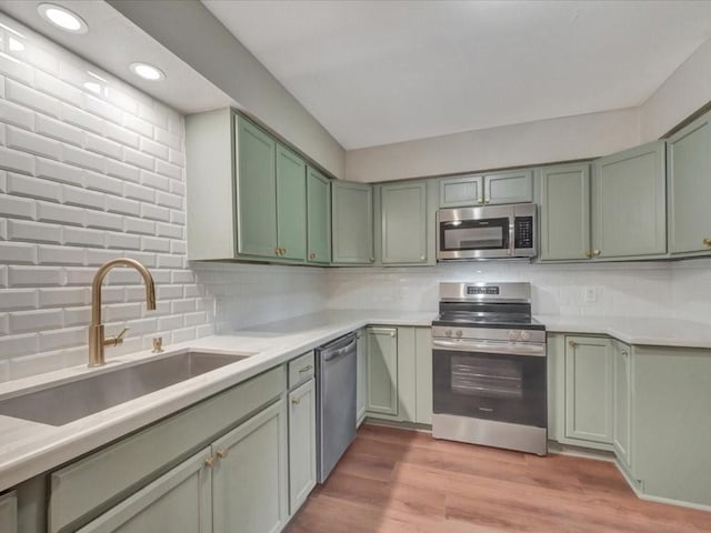 kitchen with decorative backsplash, appliances with stainless steel finishes, a sink, light countertops, and green cabinetry